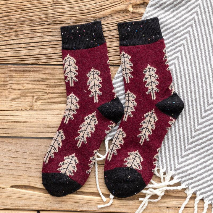 Pair of burgundy socks with beige leaf pattern, black cuffs and toes, on wooden surface and gray striped fabric