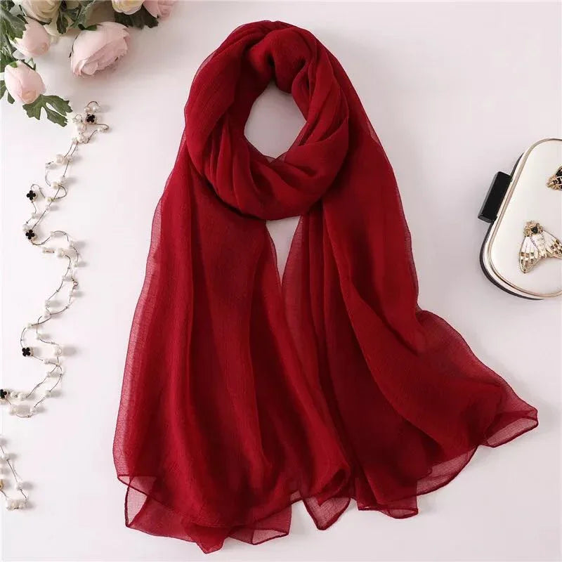 Elegant deep red chiffon scarf displayed with pink roses, delicate pearl necklace, and white clutch
