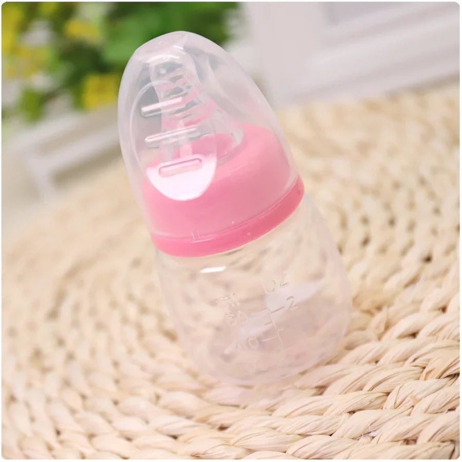 Clear baby bottle with pink lid and nipple on woven beige surface