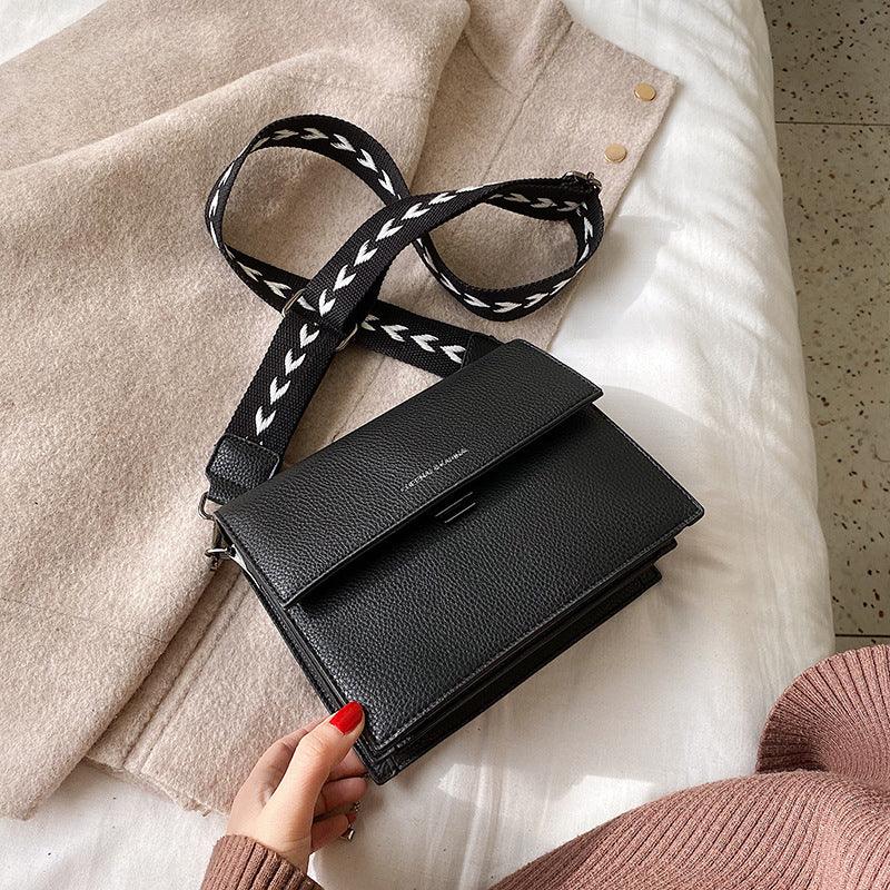 Black leather crossbody bag with white chevron patterned strap on beige and white fabric background