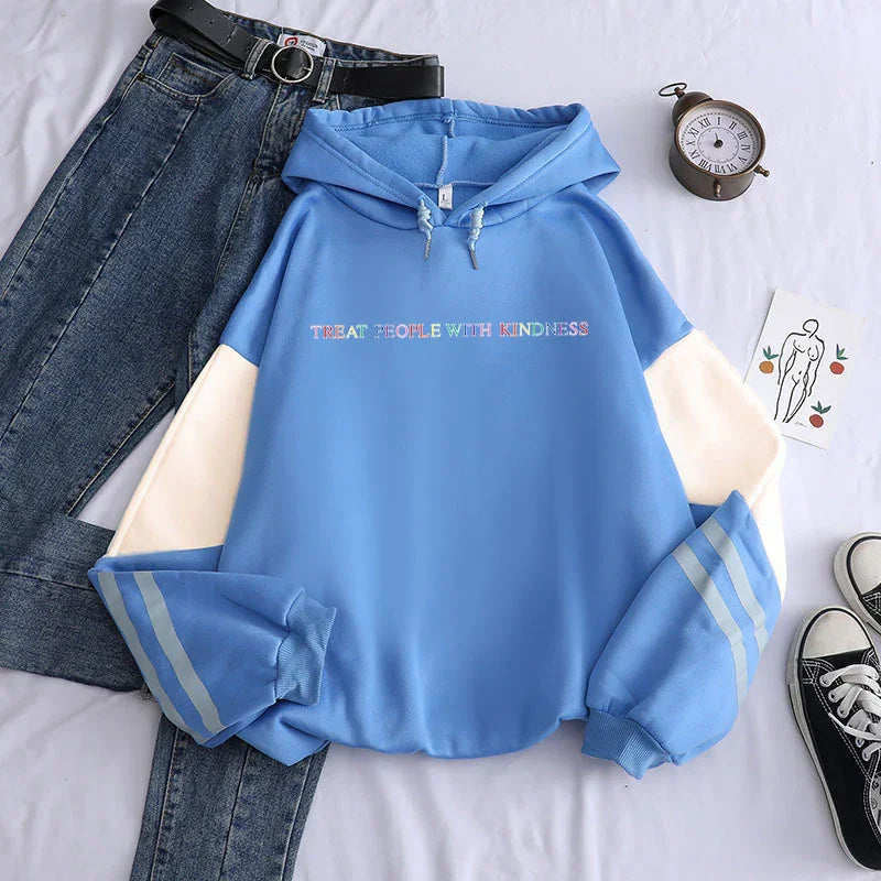 Blue hoodie with cream sleeves and 'Treat People With Kindness' text, paired with jeans and sneakers