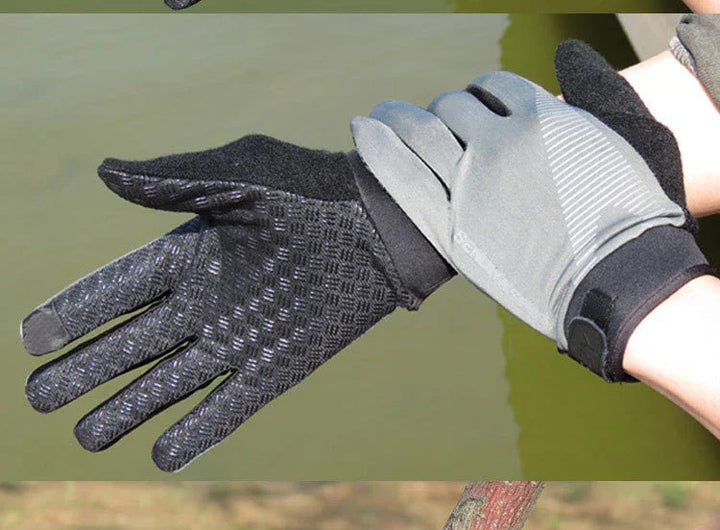 Pair of black and gray textured outdoor gloves worn on hands against a natural green and brown background