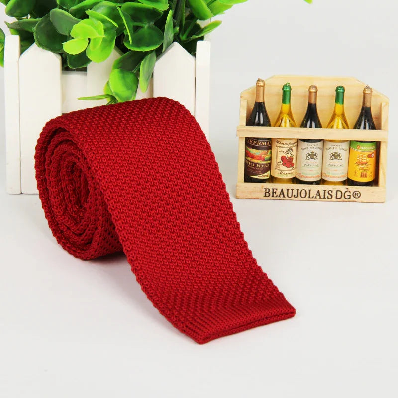 Rolled red knitted tie next to miniature wine bottles and green potted plant on white surface
