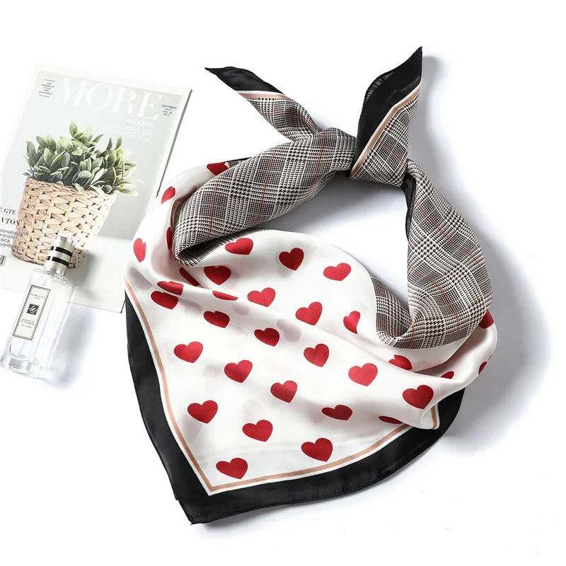 Stylish silk scarf with red heart and plaid patterns, placed next to a magazine and perfume bottle