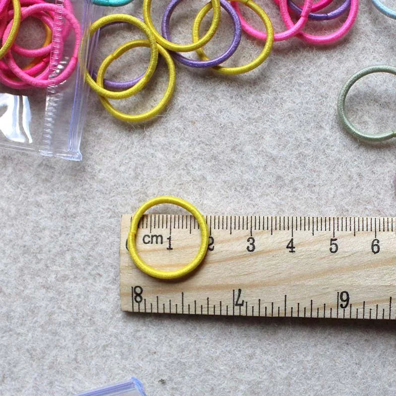Colorful hair elastic bands near wooden ruler measuring one band around 3 cm on textured surface