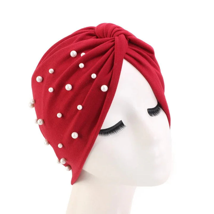 Red turban headwrap adorned with scattered white pearls on white mannequin with closed eyes