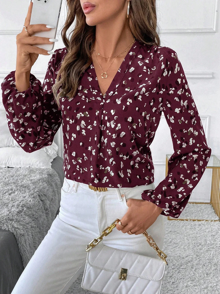 Woman wearing a burgundy floral blouse with white pants holding a white quilted handbag indoors