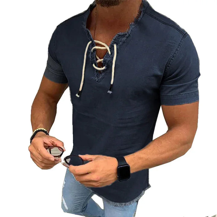 Man wearing a navy blue short-sleeve lace-up shirt holding sunglasses, paired with light ripped jeans