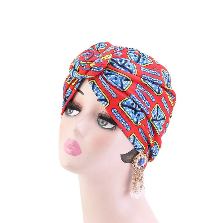 Mannequin head wearing a vibrant red and blue patterned African print turban with decorative tassel earrings