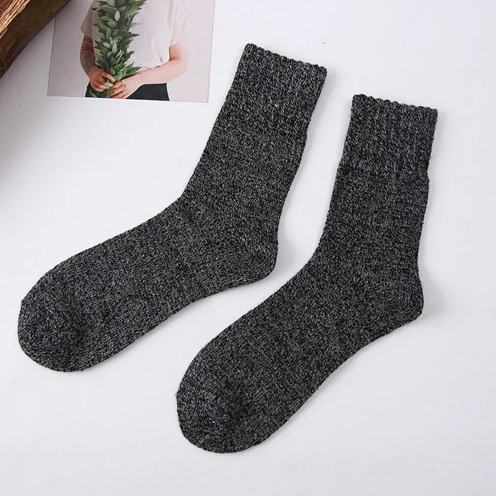 Pair of black and gray knit wool socks laid flat on white surface with partial photo background