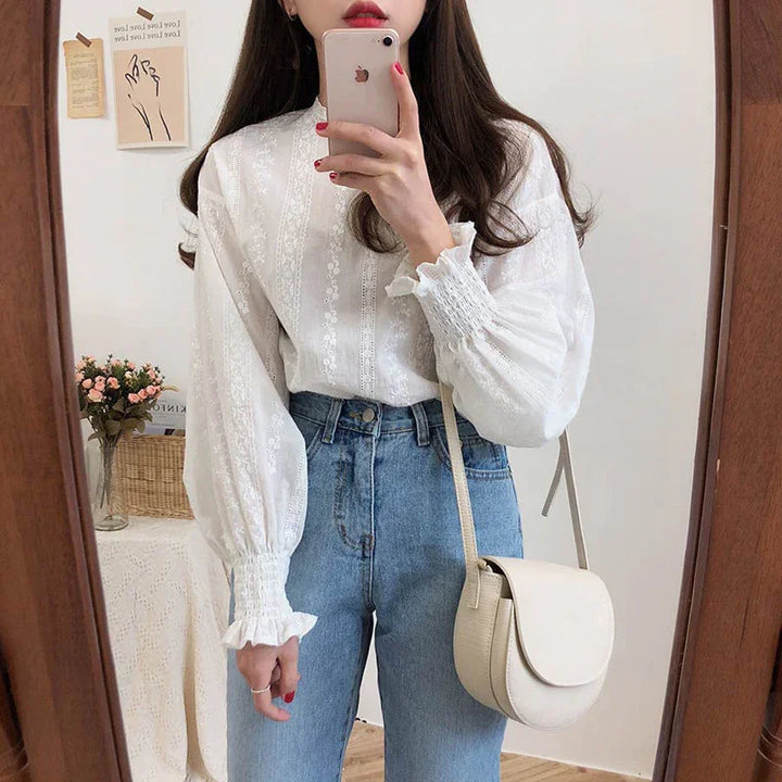 Woman wearing white lace blouse and blue jeans taking mirror selfie with beige crossbody bag