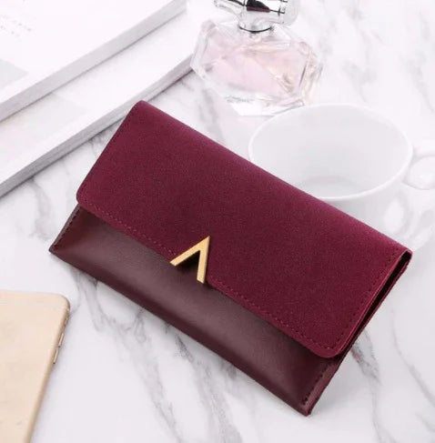 Elegant two-tone burgundy women's wallet with gold V clasp on marble surface near perfume, cup, and phone