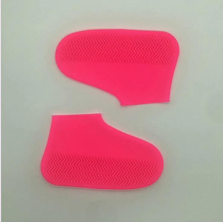 Pair of bright pink silicone shoe covers with textured zigzag soles on a light background