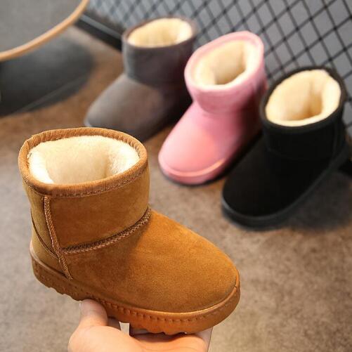 Hand holding brown suede winter boots with plush lining, other boots in gray, pink, and black in background.