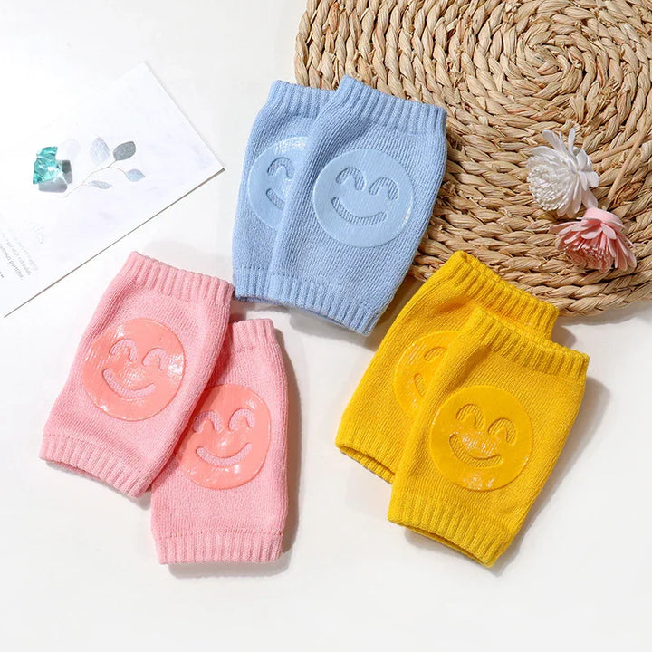 Colorful knitted baby knee pads in pink, blue, and yellow with smiling face prints on white background