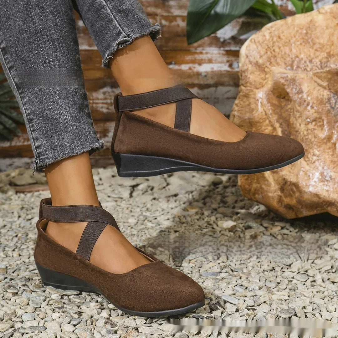 Woman wearing brown wedge shoes with elastic ankle straps, paired with frayed gray jeans on gravel surface