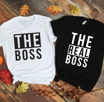 White and black t-shirts on wooden floor with fall leaves; white says THE BOSS, black says THE REAL BOSS