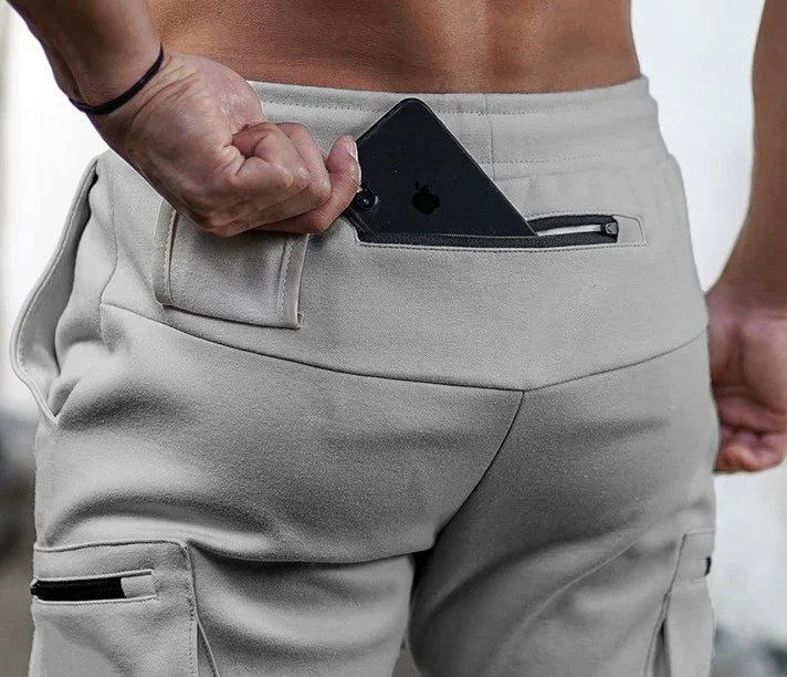 Close-up of a person placing a black iPhone into the back zippered pocket of light gray cargo pants