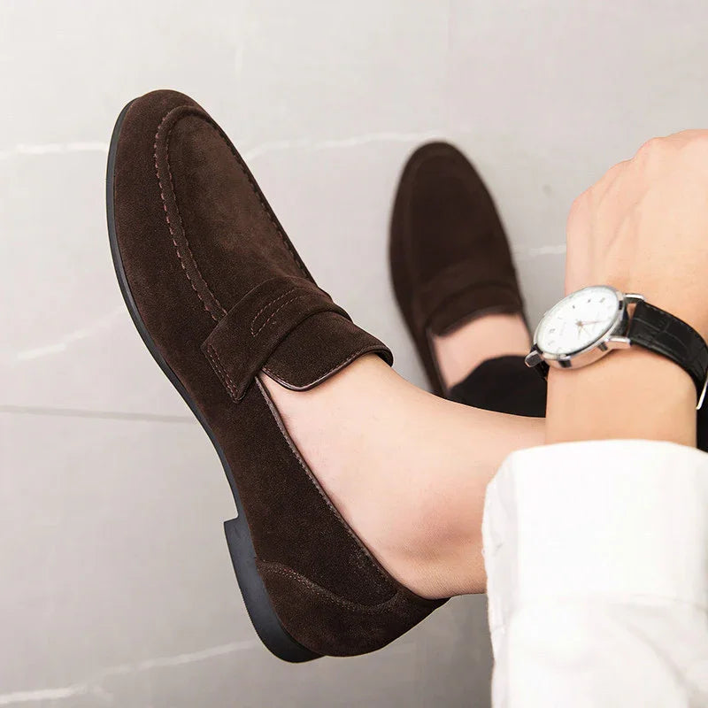 Person wearing dark brown suede loafers and a black leather watch on a tiled floor