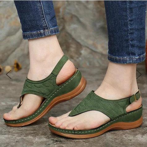 Comfortable green casual sandals with thick brown soles worn with blue jeans on stone floor