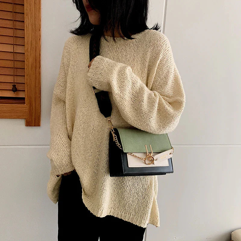 Woman wearing oversized beige knit sweater and carrying stylish green and black crossbody bag indoors
