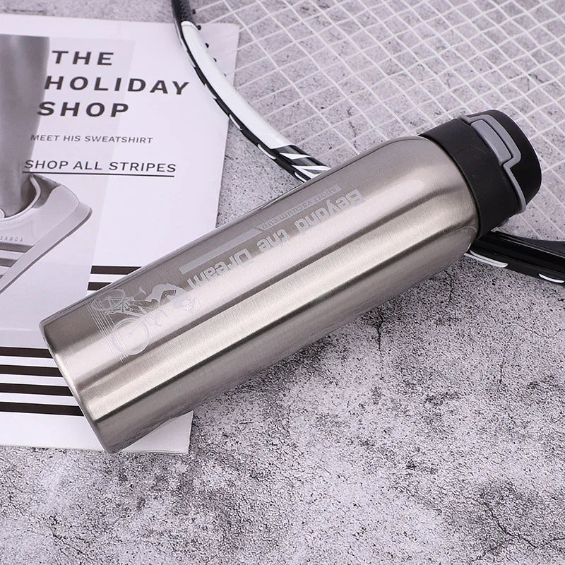 Stainless steel sports water bottle on grey surface with badminton racket and magazine