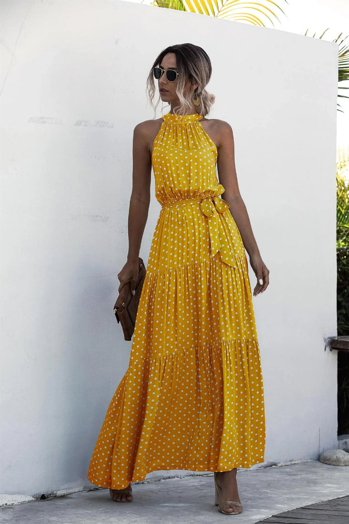 Woman wearing a yellow polka dot halter neck maxi dress with a waist tie and sunglasses outdoors