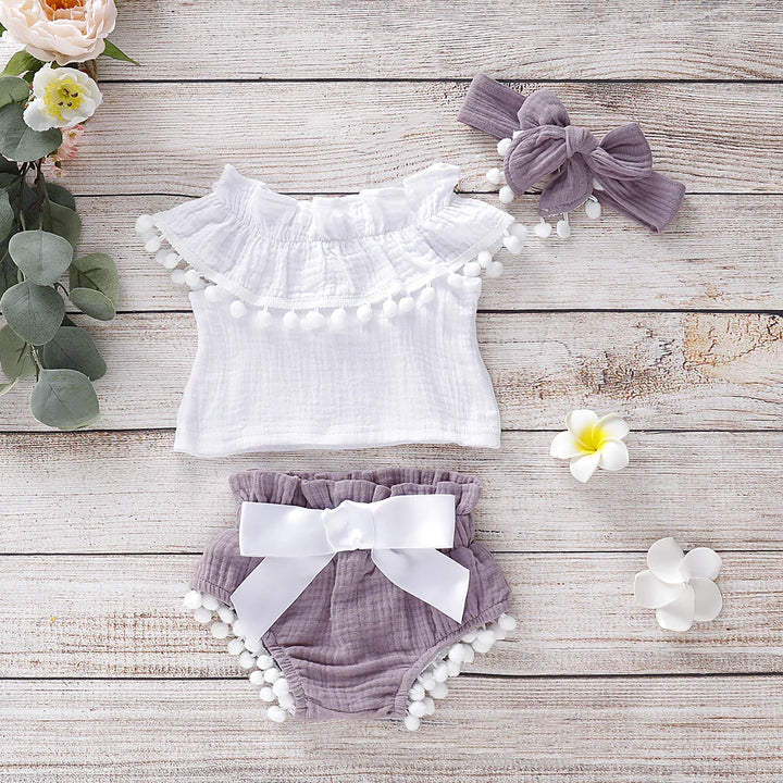 Baby girl summer outfit set with white ruffle top, purple bloomers, and matching bow headband on wooden background