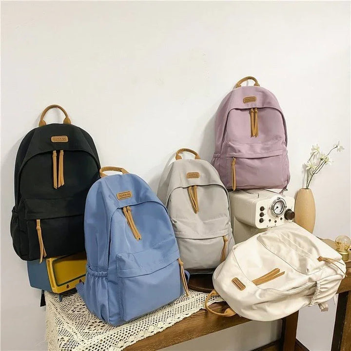 Five stylish nylon backpacks in black, blue, gray, purple, and white displayed on a wooden table with vintage decor