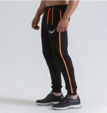 Man wearing black jogger pants with orange side stripes and orange drawstrings, paired with black sneakers