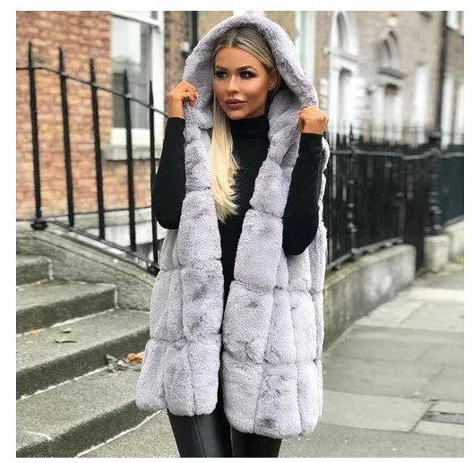 Woman wearing a stylish light gray hooded faux fur vest over black outfit, standing on city sidewalk