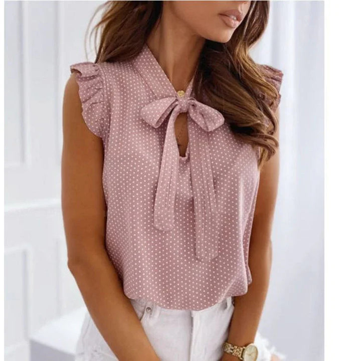 Woman wearing sleeveless mauve polka dot blouse with bow tie neck and ruffled shoulders