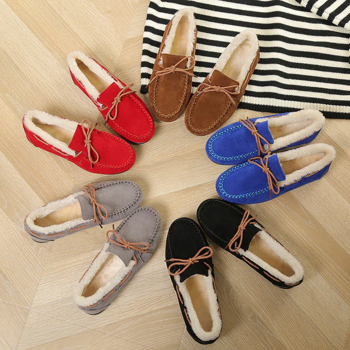 Circle of cozy moccasin slippers in red, brown, blue, black, and gray with fur lining on wooden floor