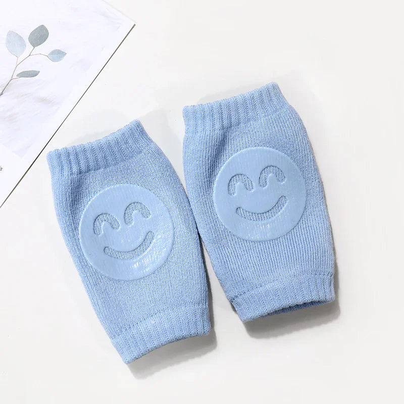Light blue knit baby knee pads with smiling face anti-slip grips on a white surface