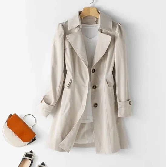Beige trench coat with large buttons and lapel collar displayed on hanger over white shirt, paired with stylish orange and white handbag