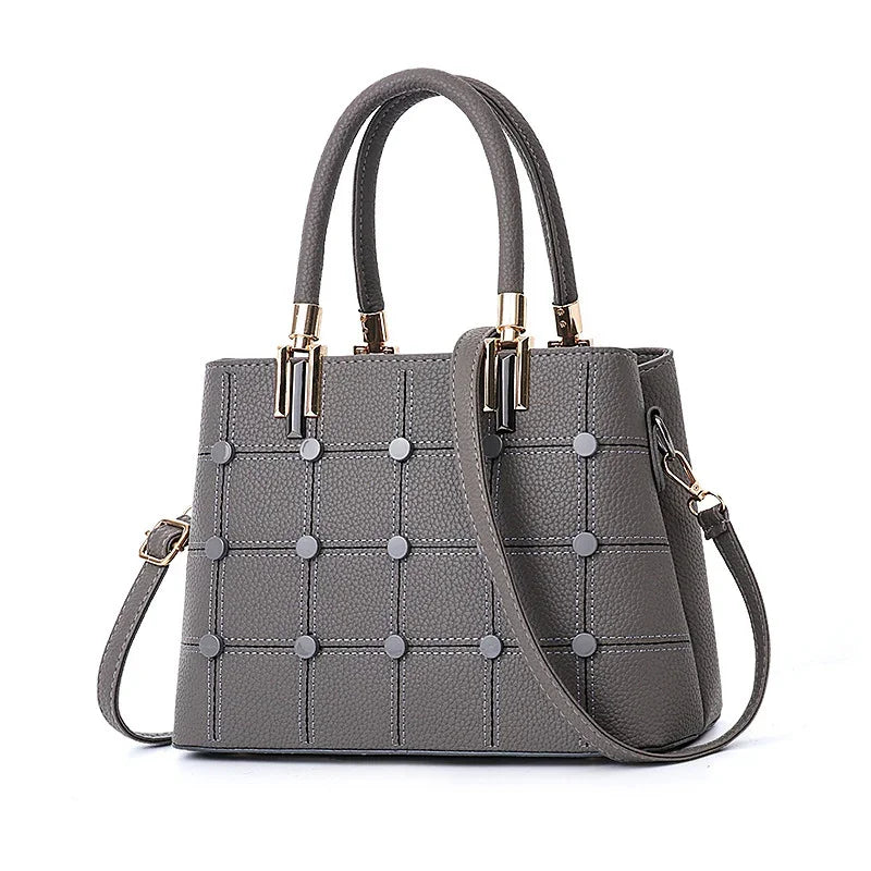 Gray leather handbag with grid pattern and circular studs, featuring dual handles and a detachable shoulder strap