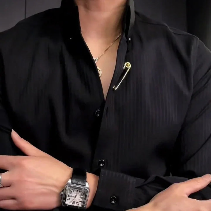 Person wearing black shirt with gold safety pin and chain necklace, silver watch with black leather strap