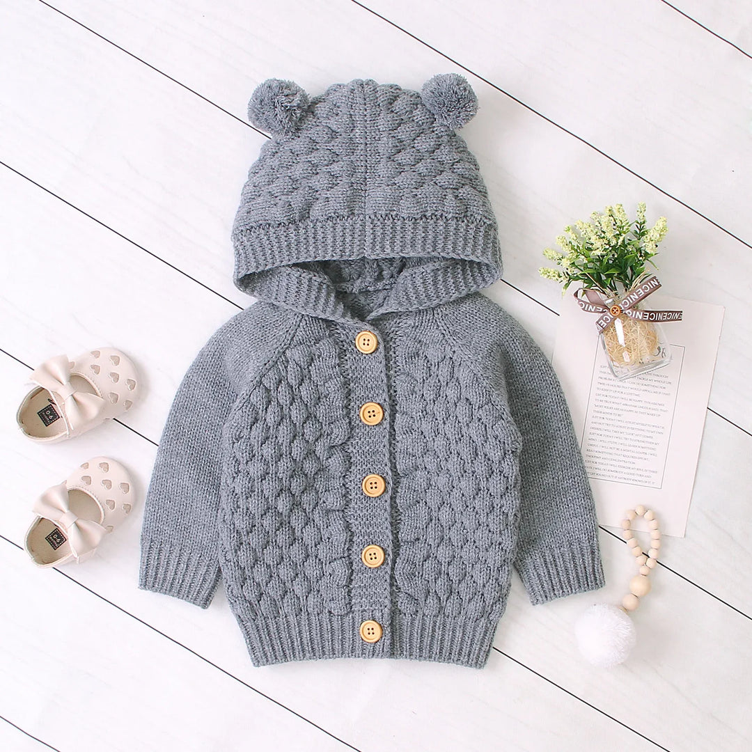 Gray knitted baby cardigan with hood and bear ears, wooden buttons, paired with cream shoes and small flowers