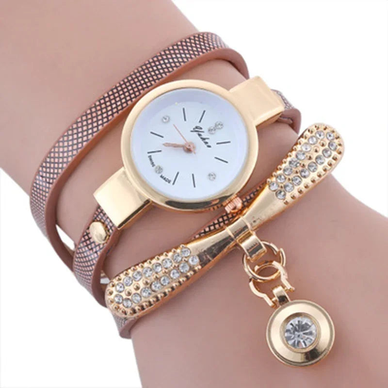 Elegant gold wristwatch with white dial and crystal markers, paired with rhinestone-studded bracelet charm on pink strap