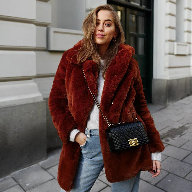 Woman wearing rust brown faux fur coat, light sweater, blue jeans, and black quilted crossbody bag on city street