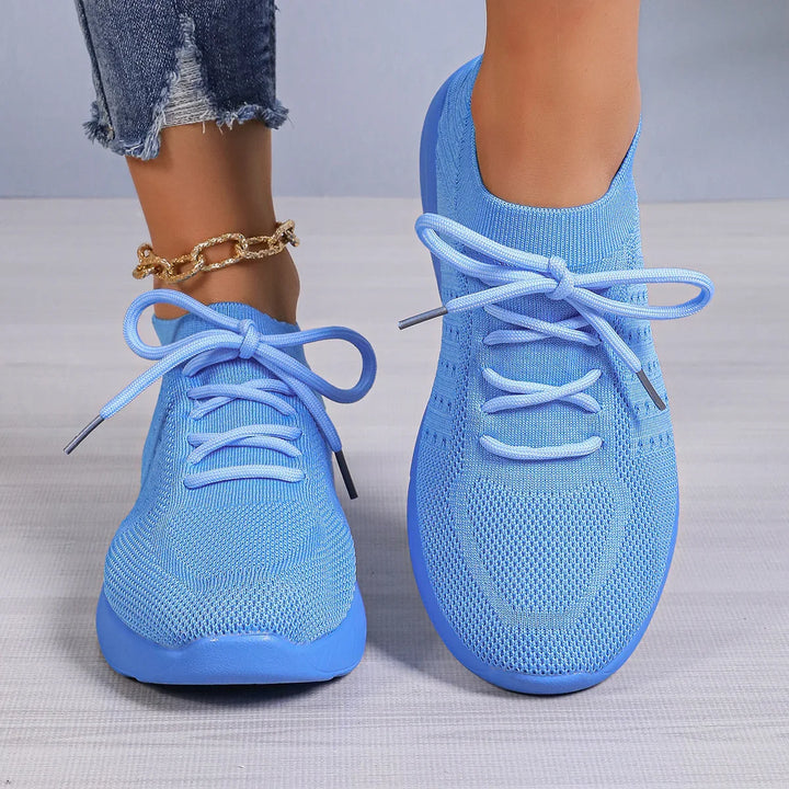 Pair of blue knit athletic sneakers with laces worn with rolled frayed jeans and gold chain anklet