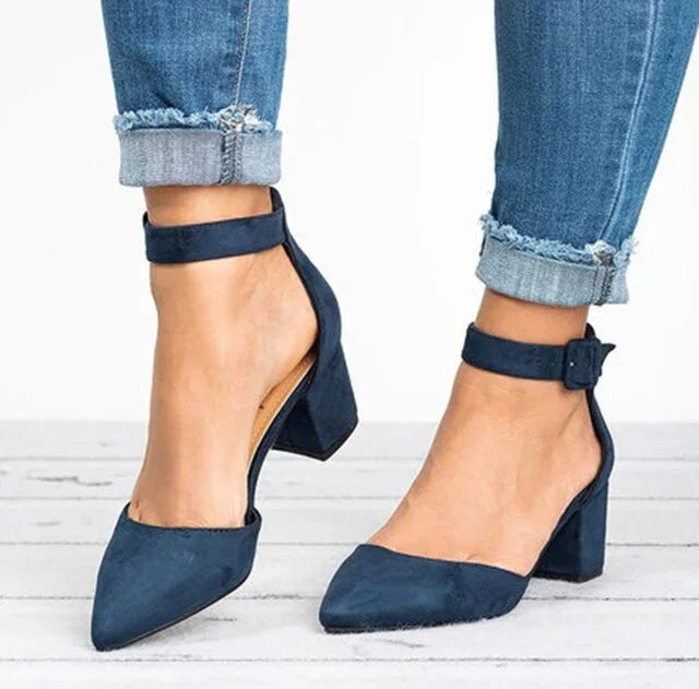 Women's navy blue block heel shoes with ankle straps worn with cuffed blue jeans on wooden floor