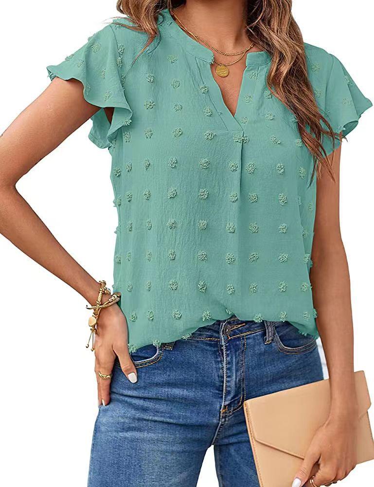 Woman wearing teal textured flutter sleeve blouse with blue jeans and holding beige clutch purse