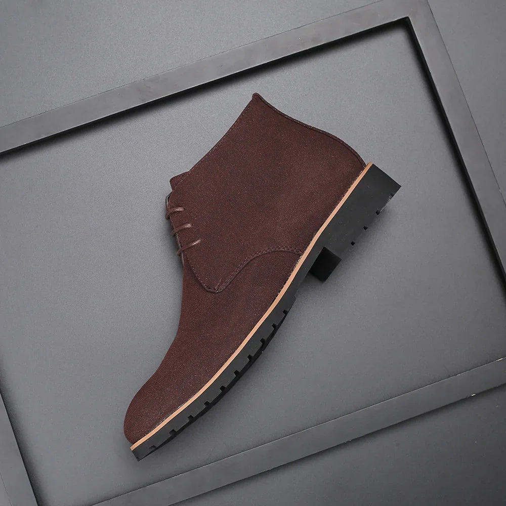 Brown suede desert boot with black rubber sole on gray background