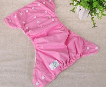 Pink reusable cloth diaper with white snap buttons on beige surface next to green plant