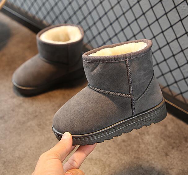 Hand holding a gray suede winter boot with plush lining on a carpeted floor