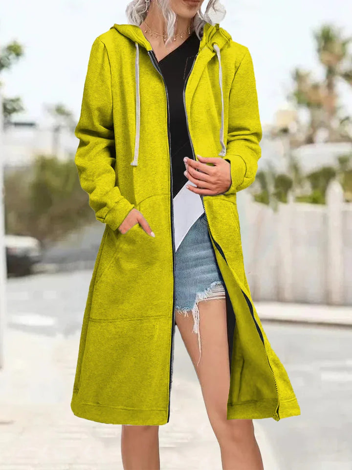 Woman wearing bright yellow long zip-up hoodie with hood and pockets over casual black top and ripped denim shorts outdoors