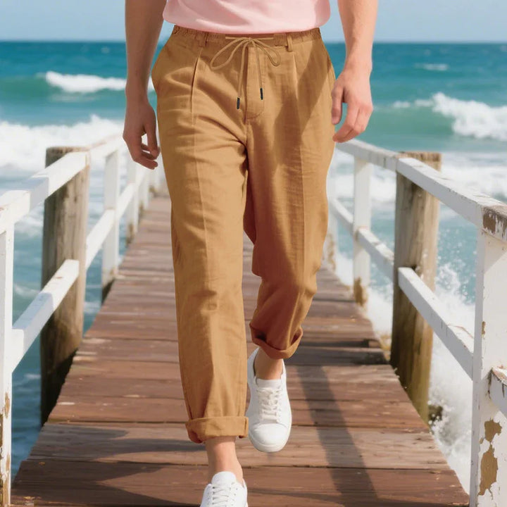 Person wearing tan linen pants and white sneakers walking on wooden pier by ocean