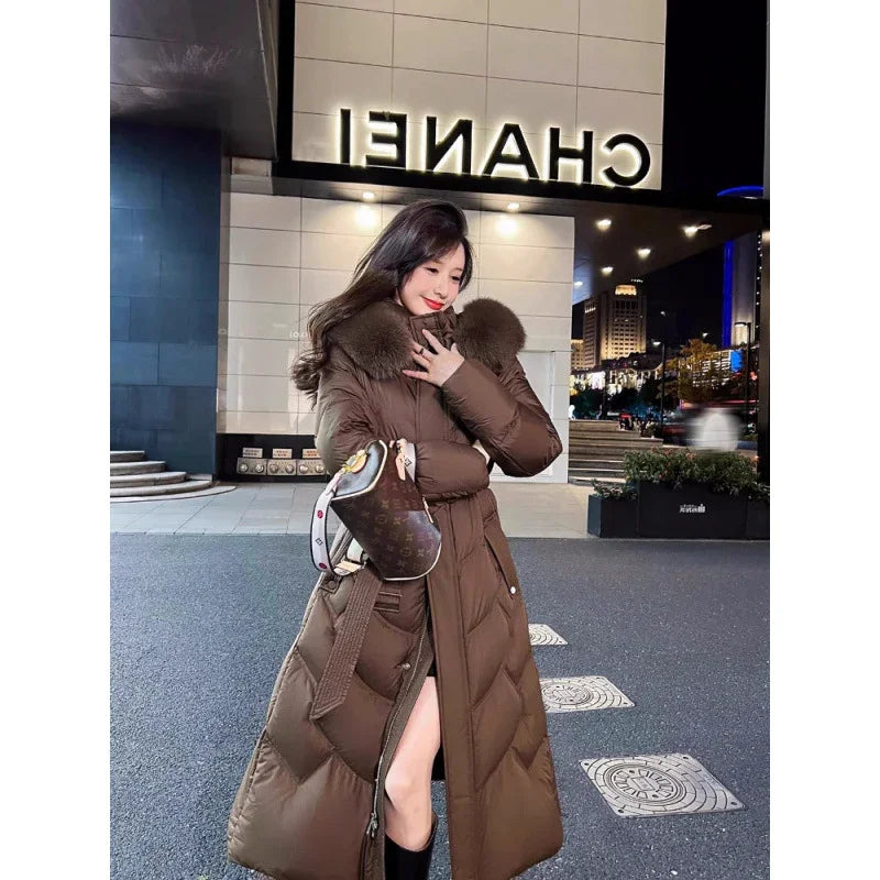 Woman in long brown puffer coat with fur collar and designer handbag outside Chanel store at night