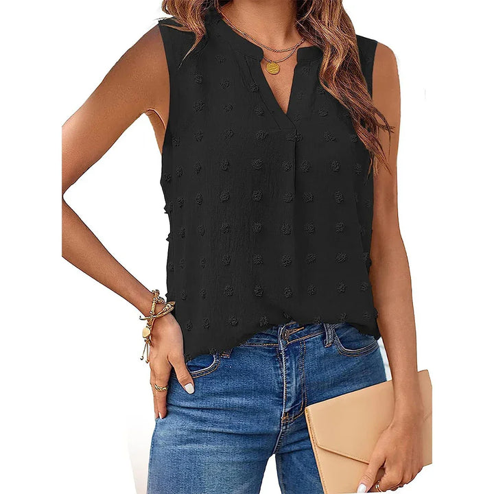 Woman wearing sleeveless black textured blouse with V-neck paired with blue jeans and holding beige clutch